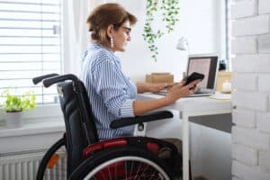 woman-wearing-glasses-in-wheelchair-at-desk-with-phone-and-laptop