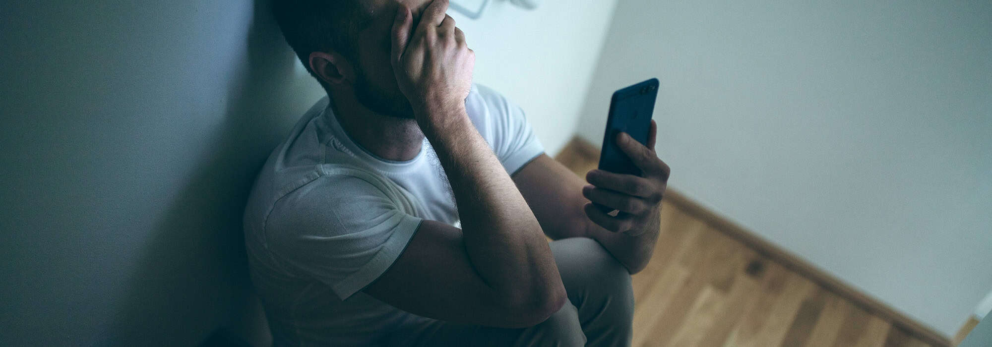 depressed man sitting on a stair case looking at his phone